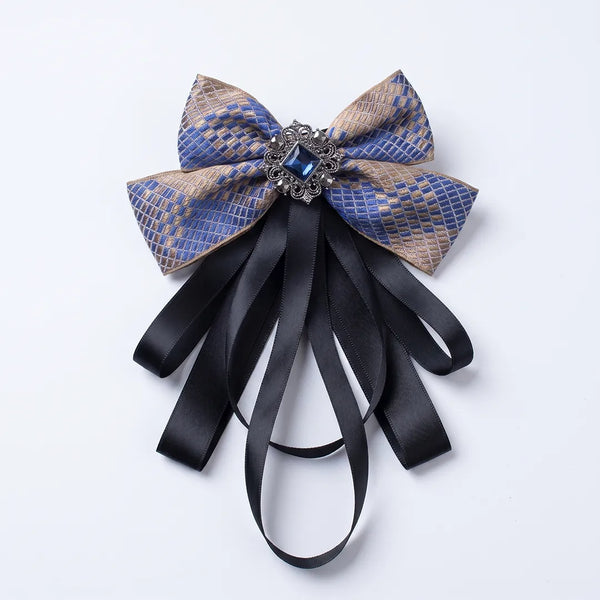 Close-up of a luxurious blue and gold checkered silk bow tie featuring cascading black ribbon tails and an ornate square blue crystal brooch.