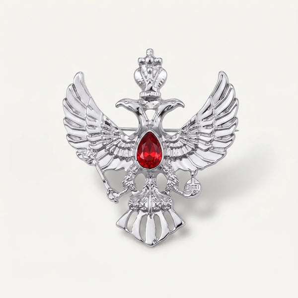 Close-up of a polished silver-tone double-headed eagle crest collar pin featuring a crown, scepter, orb, and a ruby-red center stone.
