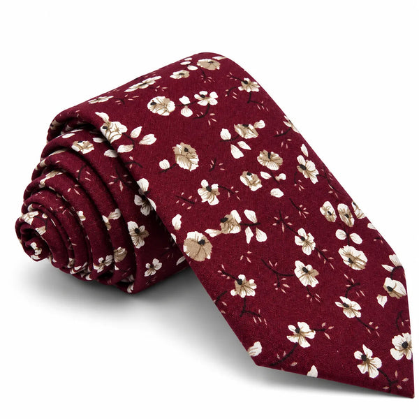 A burgundy necktie with a delicate white and beige floral pattern, shown rolled on the left and laid flat on the right against a clean white background.