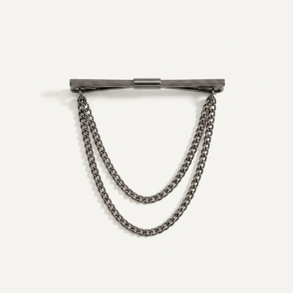 Close-up of a polished dark gunmetal horizontal collar pin with a diamond-knurled texture and two tiered, draped curb chains.