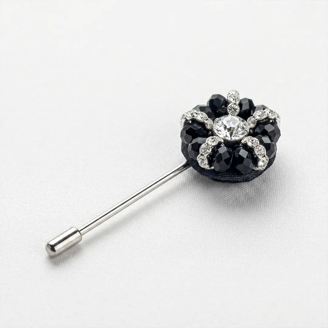 Close-up of a black and crystal flower lapel pin featuring a central clear crystal surrounded by faceted black petals and sparkling accents on a silver-tone stem.