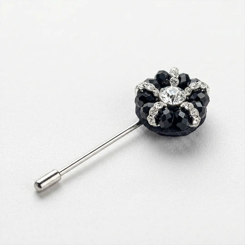 Close-up of a black and crystal flower lapel pin featuring a central clear crystal surrounded by faceted black petals and sparkling accents on a silver-tone stem.