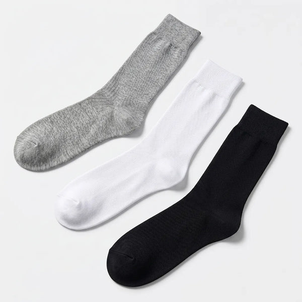 Flat lay of a 3-pack of men's solid crew socks in light grey, white, and black.
