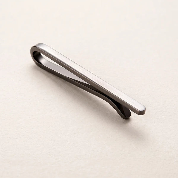 Close-up of a minimalist brushed silver metal tie clip on a neutral background.