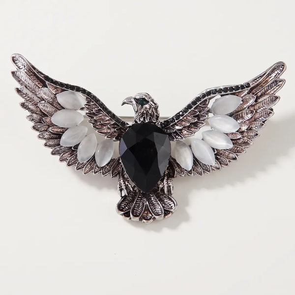 Close-up of an antiqued silver-tone eagle crest collar pin featuring a large faceted black center stone, milky white wing stones, and a green eye.