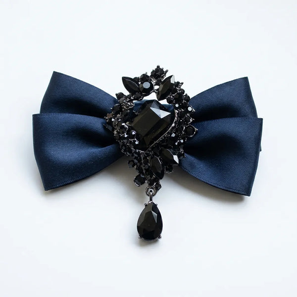 Close-up of a luxurious solid navy blue silk bow tie featuring an elaborate black onyx crystal brooch centerpiece with a dangling teardrop gem.
