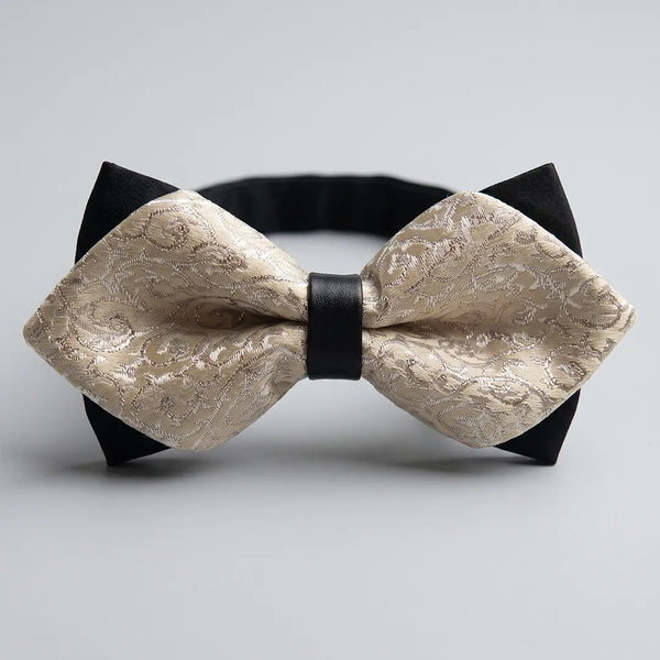 Close-up of a champagne beige jacquard paisley diamond bow tie featuring sharp pointed edges, black backing tips, and a black center knot on a smooth polyester fabric.