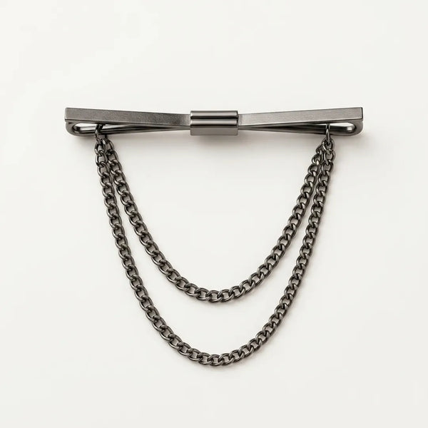 Close-up of a polished dark gunmetal flat bar collar pin with a smooth satin-brushed finish and two tiered, draped curb chains.