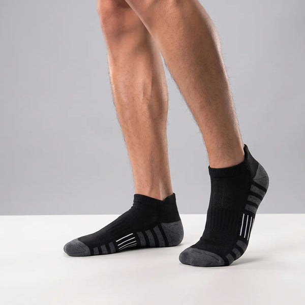 Close-up of a man's feet wearing black sport ankle socks with grey heel and toe caps and grey-and-white side stripes.
