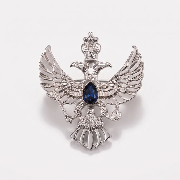 Close-up of a polished silver-tone double-headed eagle crest collar pin featuring a crown, scepter, orb, and a sapphire-blue center stone.