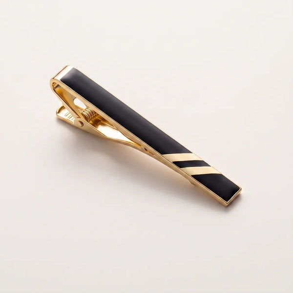 Close-up of a black and gold striped tie clip featuring a spring-loaded metal mechanism and a sleek black enamel inlay.
