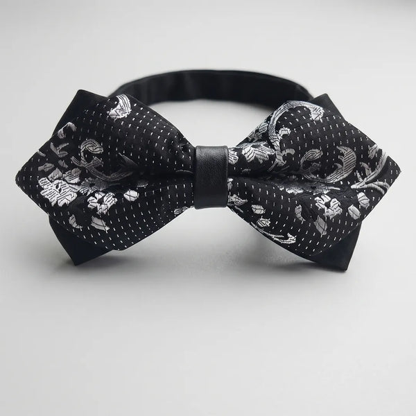 Close-up of a black and silver floral jacquard diamond bow tie featuring stitched micro-dots and a solid black center knot on a smooth polyester fabric.