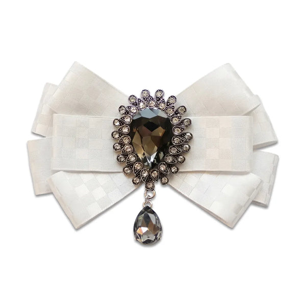 Close-up of a luxurious white silk bow tie featuring a subtle checkered pattern and an ornate crystal brooch centerpiece with a dark dangling teardrop gem.