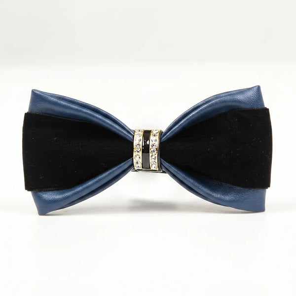 Close-up of a luxurious two-tone navy blue leather and black bow tie featuring a gold metallic ring centerpiece encrusted with clear crystals and black enamel.