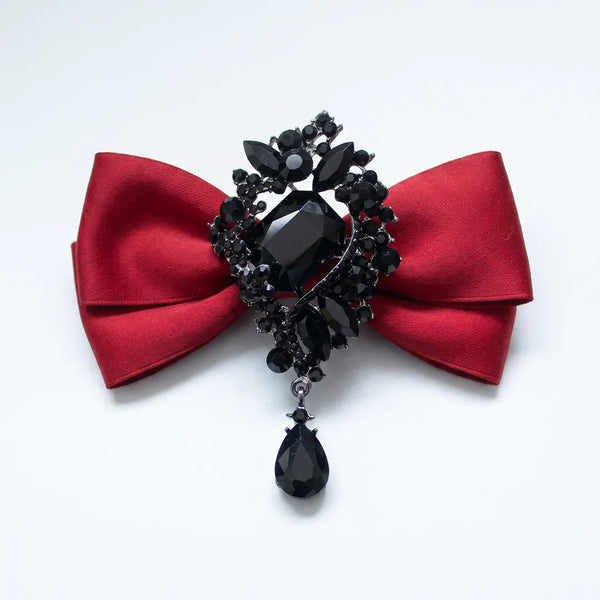Close-up of a luxurious solid red silk bow tie featuring an elaborate black onyx crystal brooch centerpiece with a dangling teardrop gem.