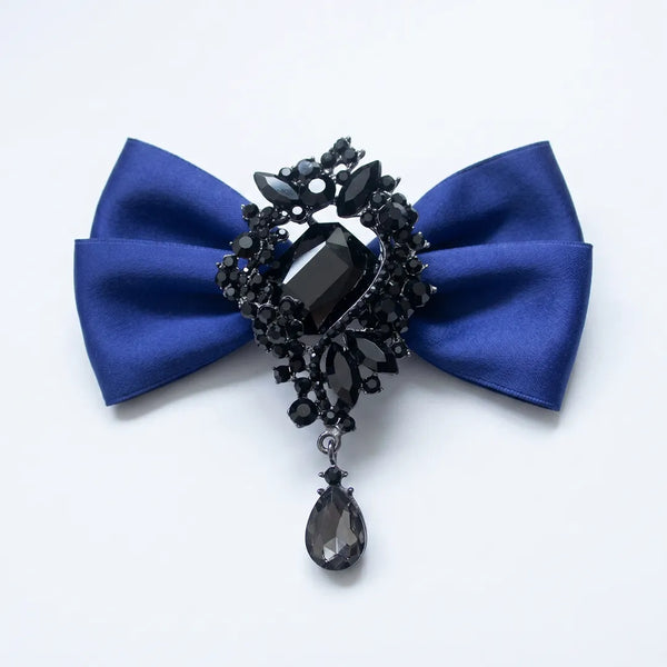 Close-up of a luxurious solid royal blue silk bow tie featuring an elaborate black onyx crystal brooch centerpiece with a dangling teardrop gem.