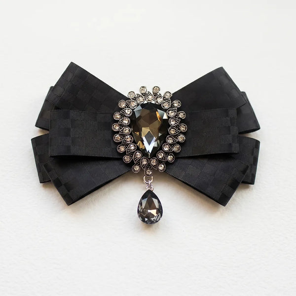 Close-up of a luxurious black silk bow tie featuring a subtle checkered pattern and an ornate crystal brooch centerpiece with a dangling teardrop gem.