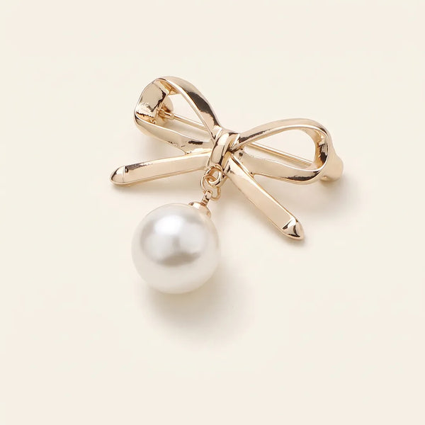 Close-up of a smooth gold-toned bow-shaped collar pin featuring a dangling white pearl.