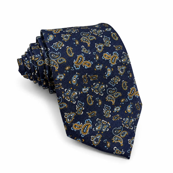 Rolled navy blue necktie featuring an all-over amber and blue paisley floral print on a white background
