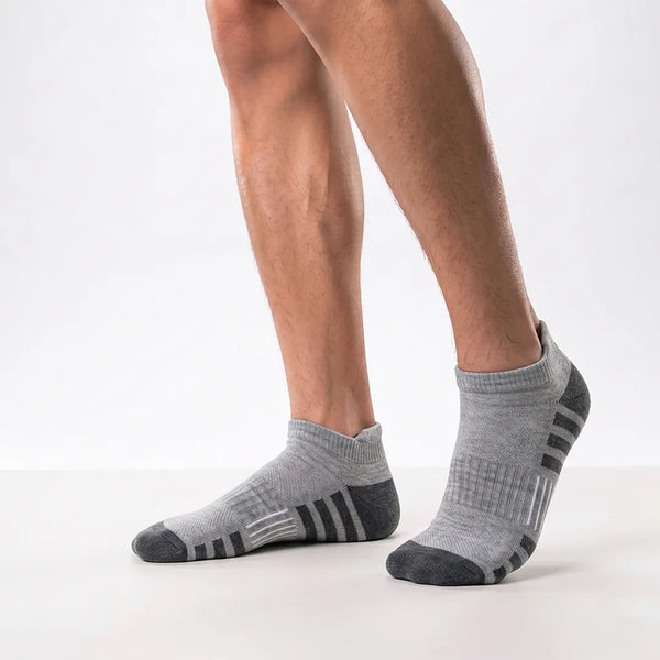 Close-up of a man's feet wearing grey sport ankle socks with dark grey heel and toe caps and striped arch accents.