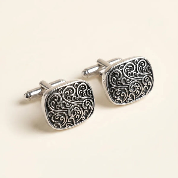 Close-up of a pair of antique silver filigree swirl cufflinks with a smooth bullet-back closure.