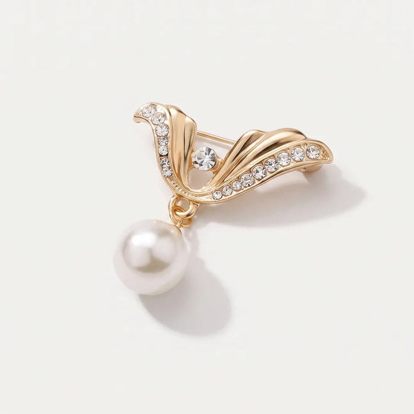 Close-up of a polished gold-tone wing-shaped collar pin accented with clear crystals and a large dangling white faux-pearl.