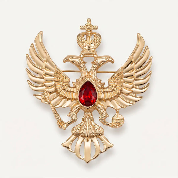Close-up of a polished gold-tone double-headed eagle crest collar pin featuring a crown, scepter, orb, and a ruby-red center stone.