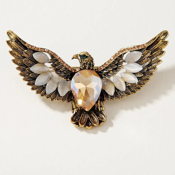 Close-up of an antiqued bronze-gold eagle crest collar pin featuring a large champagne iridescent center stone, white marquise stones, and a green eye.