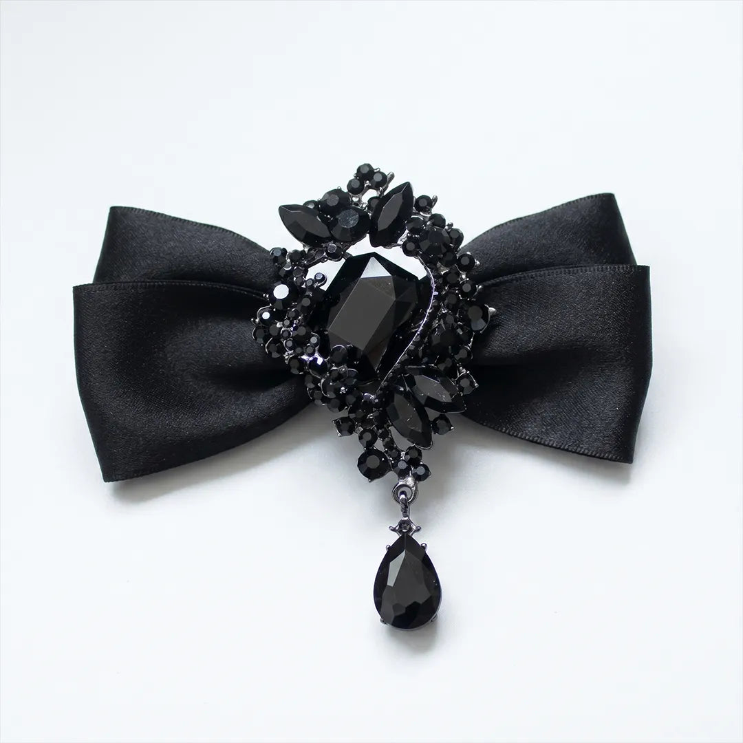 Close-up of a luxurious solid black silk bow tie featuring an elaborate black onyx crystal brooch centerpiece with a dangling teardrop gem.