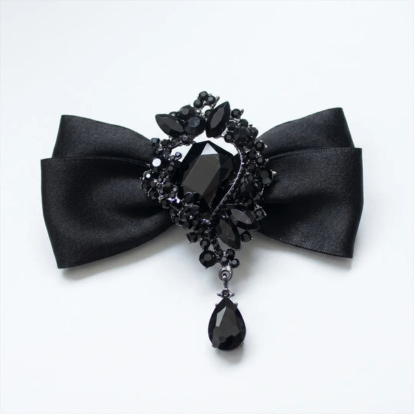 Close-up of a luxurious solid black silk bow tie featuring an elaborate black onyx crystal brooch centerpiece with a dangling teardrop gem.