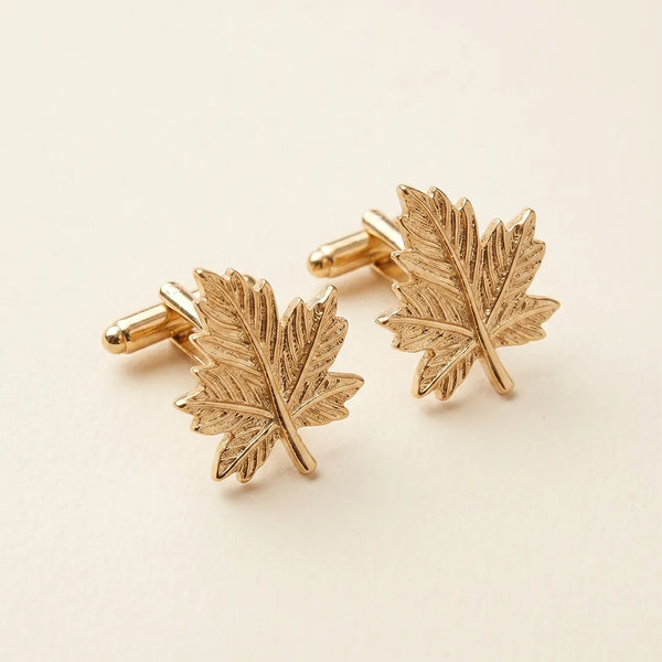 Close-up of a pair of gold-tone cufflinks sculpted into detailed maple leaf shapes.