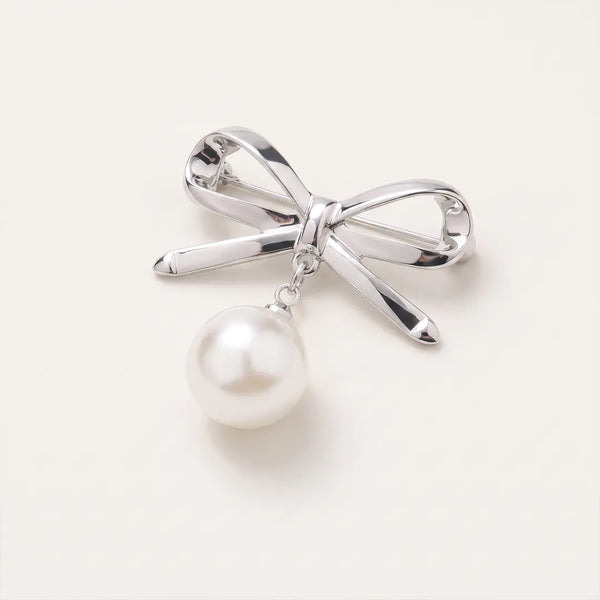 Close-up of a polished silver ribbon bow collar pin featuring a dangling white faux-pearl charm.