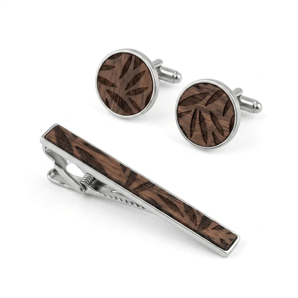 Close-up flat lay of a round silver-tone cufflink and tie clip set featuring a brown wood inlay with a leaf-geometric pattern.