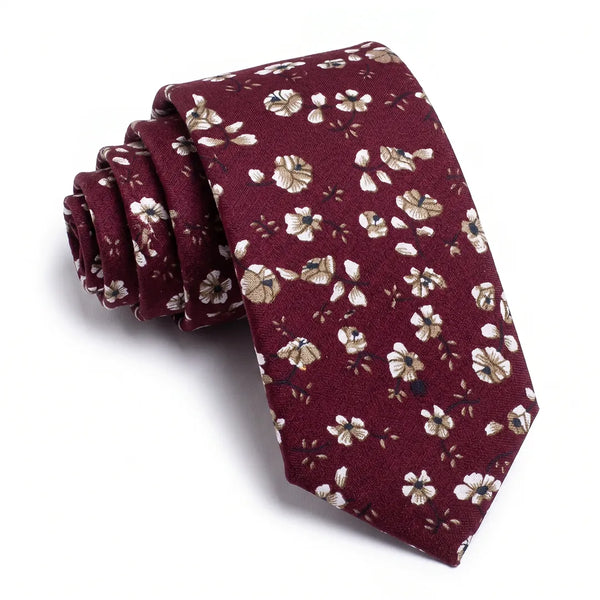 Close-up of a rolled burgundy cotton necktie featuring a ditsy floral pattern in white and cream-gold.
