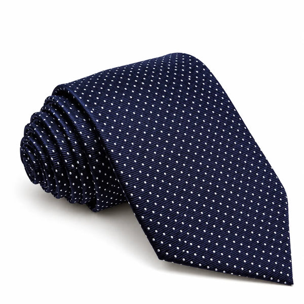A navy blue silk necktie with a small white geometric dot pattern, shown rolled on the left and laid flat on the right against a clean white background.
