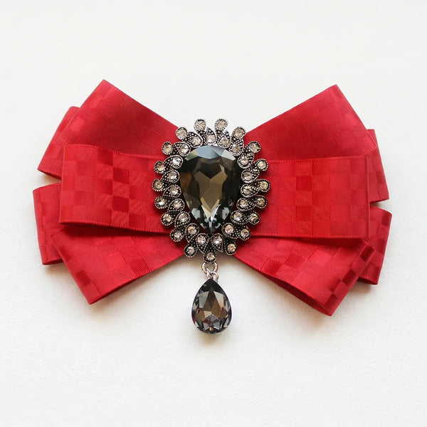 Close-up of a luxurious red silk bow tie featuring a subtle checkered pattern and an ornate crystal brooch centerpiece with a dark dangling teardrop gem.