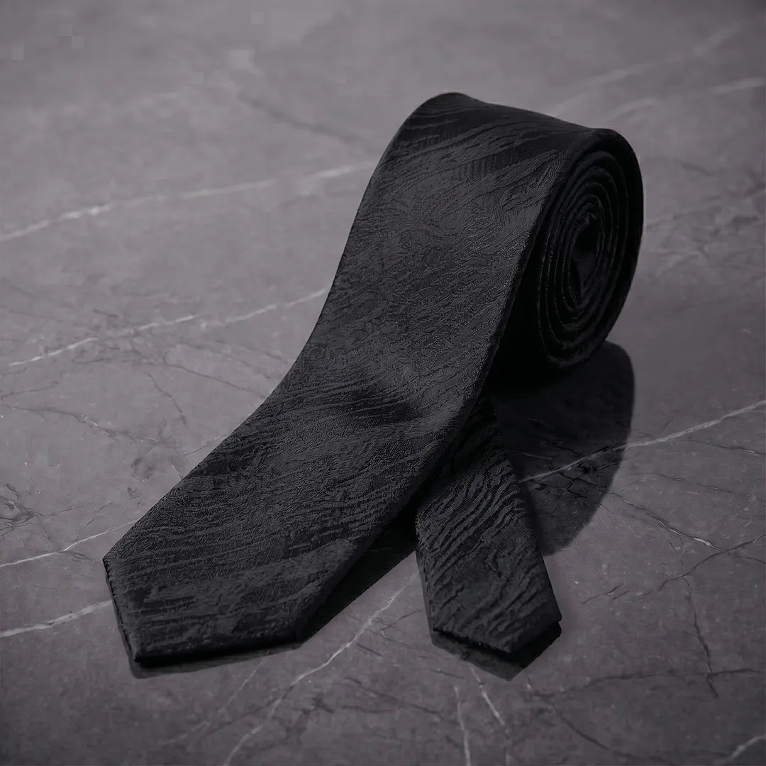 Rolled black tone-on-tone skinny tie styled on a dark marble surface.