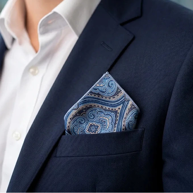 Stylish professional smiling in a navy suit and white shirt, showcasing a blue and gold paisley pocket square elegantly folded in the breast pocket.