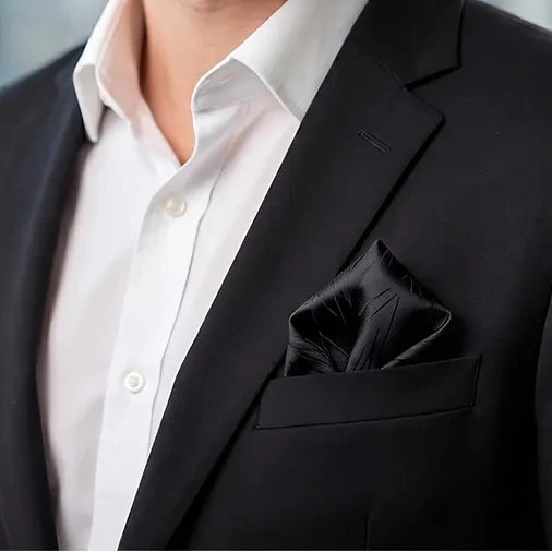 Stylish professional smiling in a black suit and white shirt, wearing a black abstract line pocket square.
