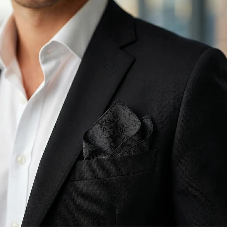 Stylish professional smiling in a black suit and white shirt, wearing a black paisley pocket square.