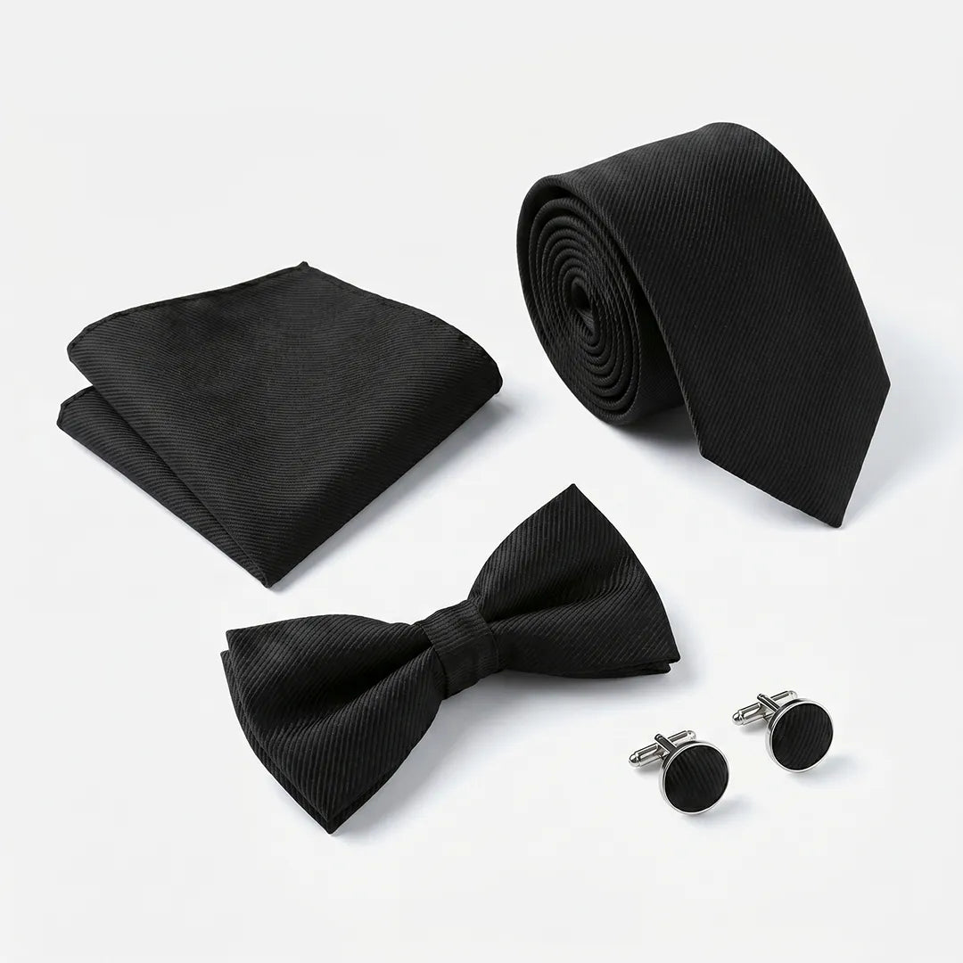 A men's formal accessory set including a black pre-tied bow tie, a matching black pocket square, a rolled black necktie, and a pair of black cufflinks with silver-toned hardware, arranged on a clean white background.