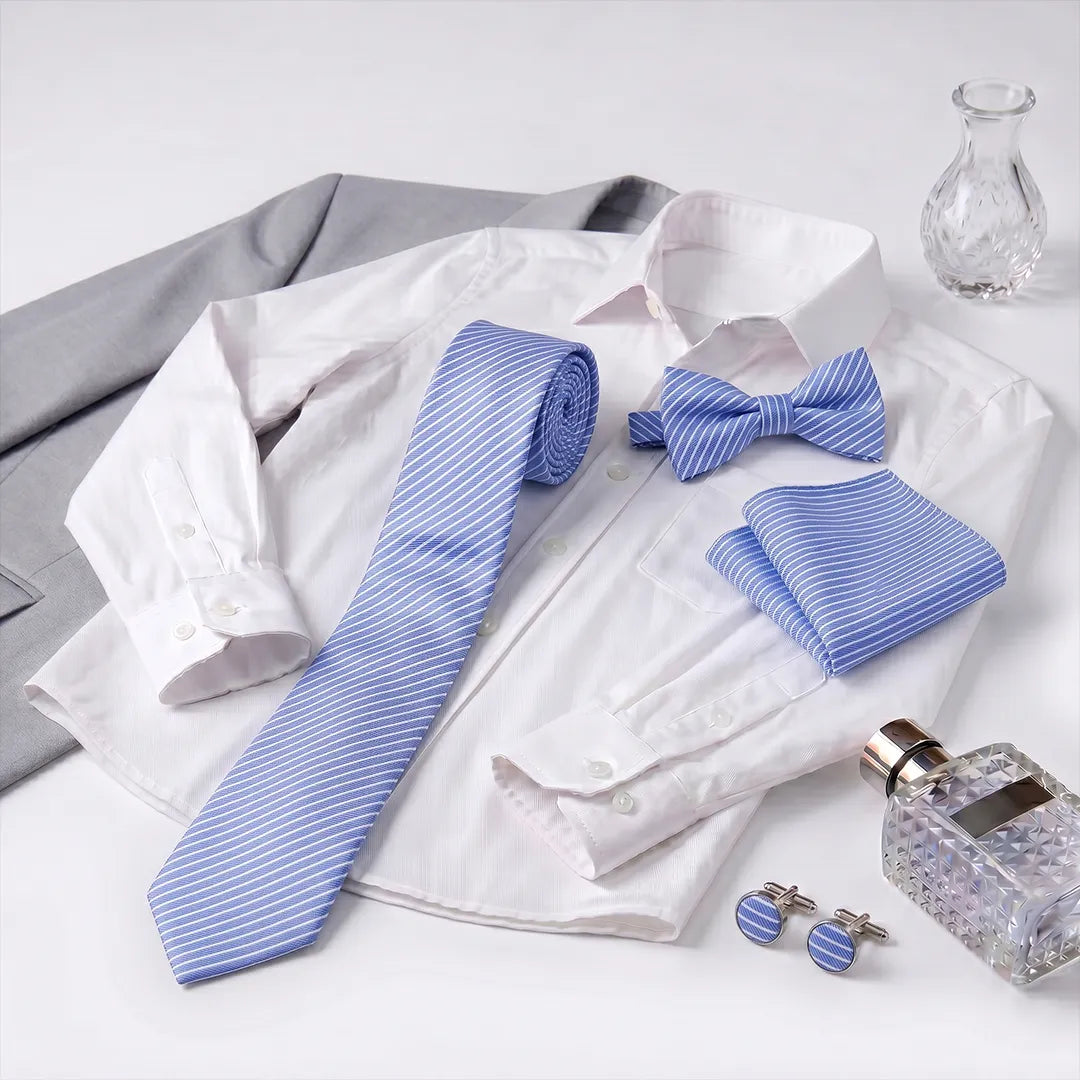 A coordinated men's formal accessory set arranged on a white dress shirt, including a blue-and-white striped necktie, matching bow tie, folded pocket square, and matching cufflinks. A gray suit jacket, a small clear glass vase, and a textured perfume bottle are also styled around the set on a white background.