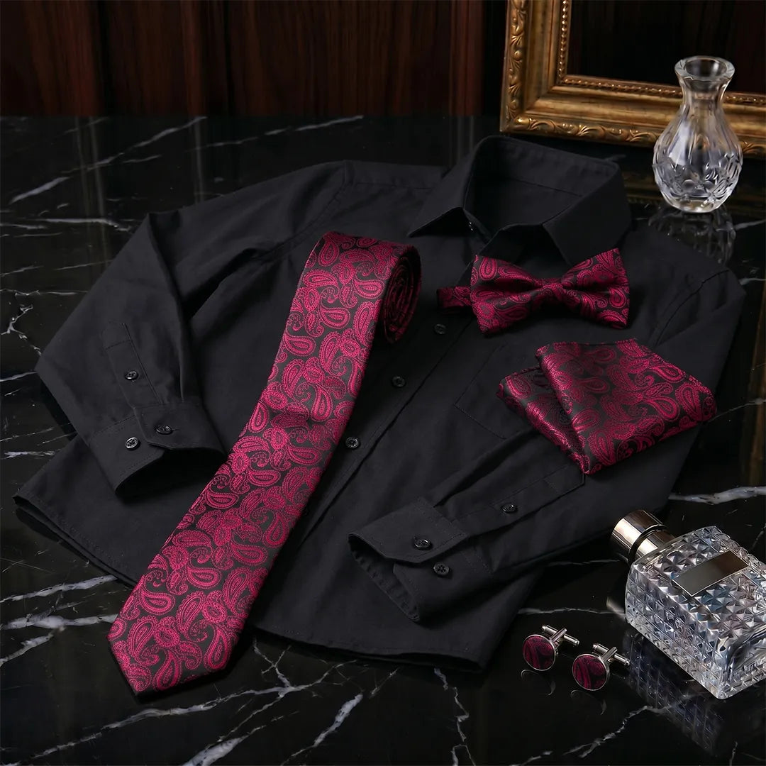 A men's formal accessory set displayed on a black dress shirt, featuring a paisley patterned tie, matching bow tie, pocket square, and cufflinks, alongside a crystal decanter and a gold-framed picture frame on a black marble surface.
