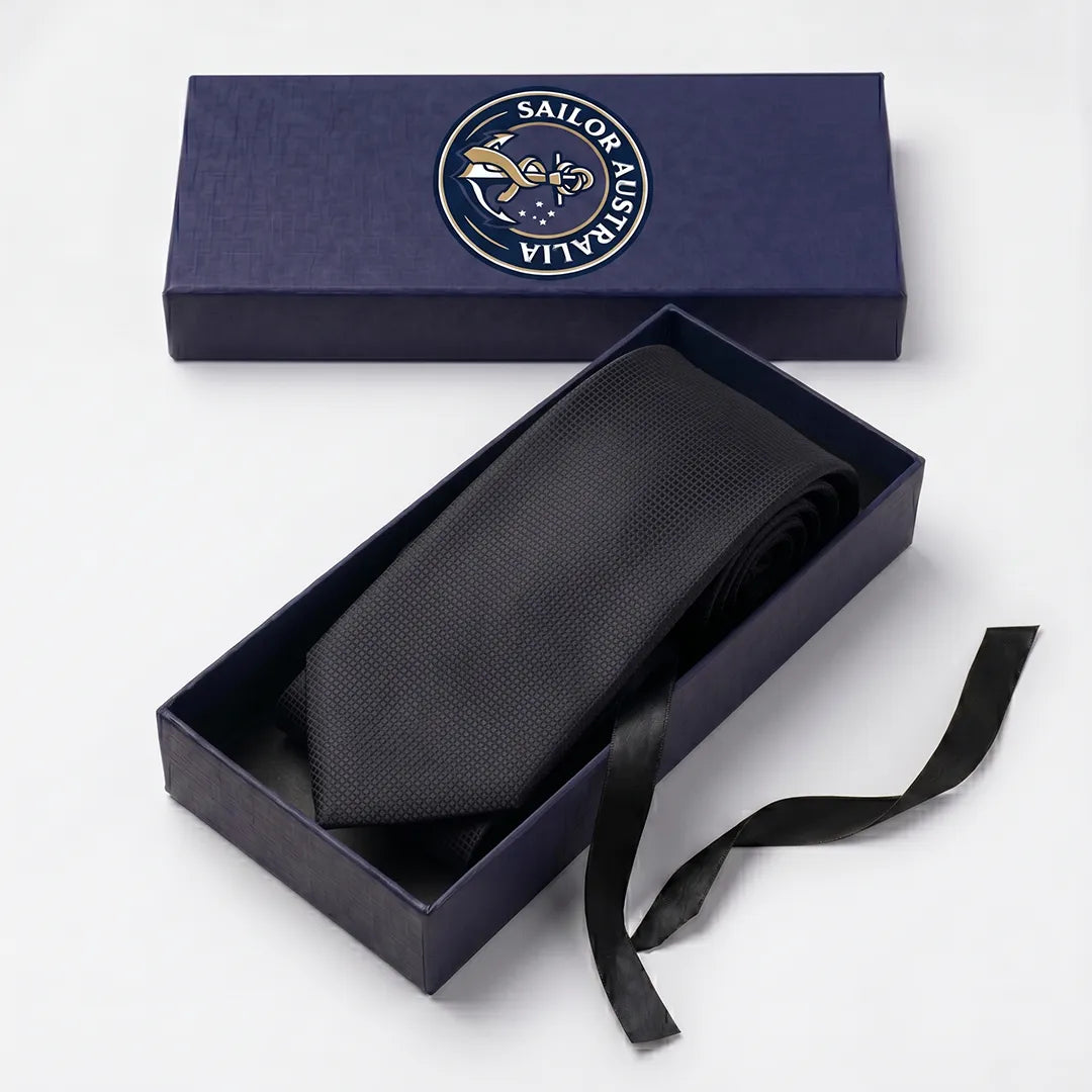 Black micro-grid necktie rolled inside an open Sailor Australia branded navy presentation gift box with black pull ribbon