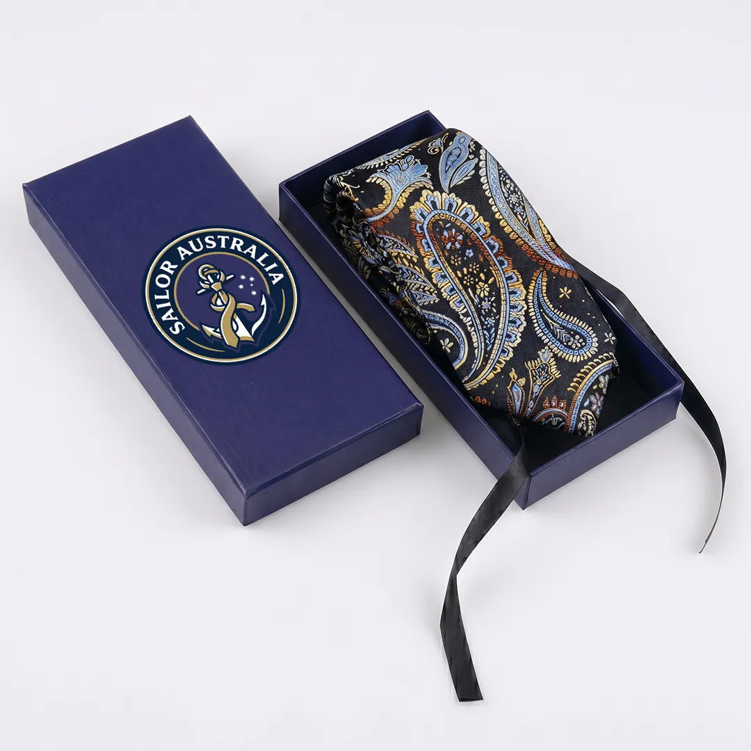 A folded paisley necktie in a dark box with its matching navy presentation box beside it. The tie has an intricate paisley pattern in blue, gold, and brown tones, and the box lid features a visible Sailor Australia logo.